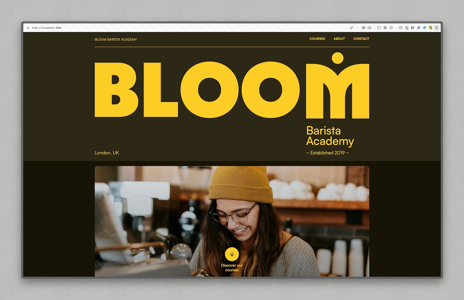 A clip of the academy website home page with a bold yellow and black colour scheme. The academy’s name, “BLOOM”,  is in large yellow letters on a black background, with the subtitle “Barista Academy” and “Established 2019” underneath. Below this, there is a photograph of a smiling barista wearing a yellow beanie and glasses, operating an espresso machine in shot too.